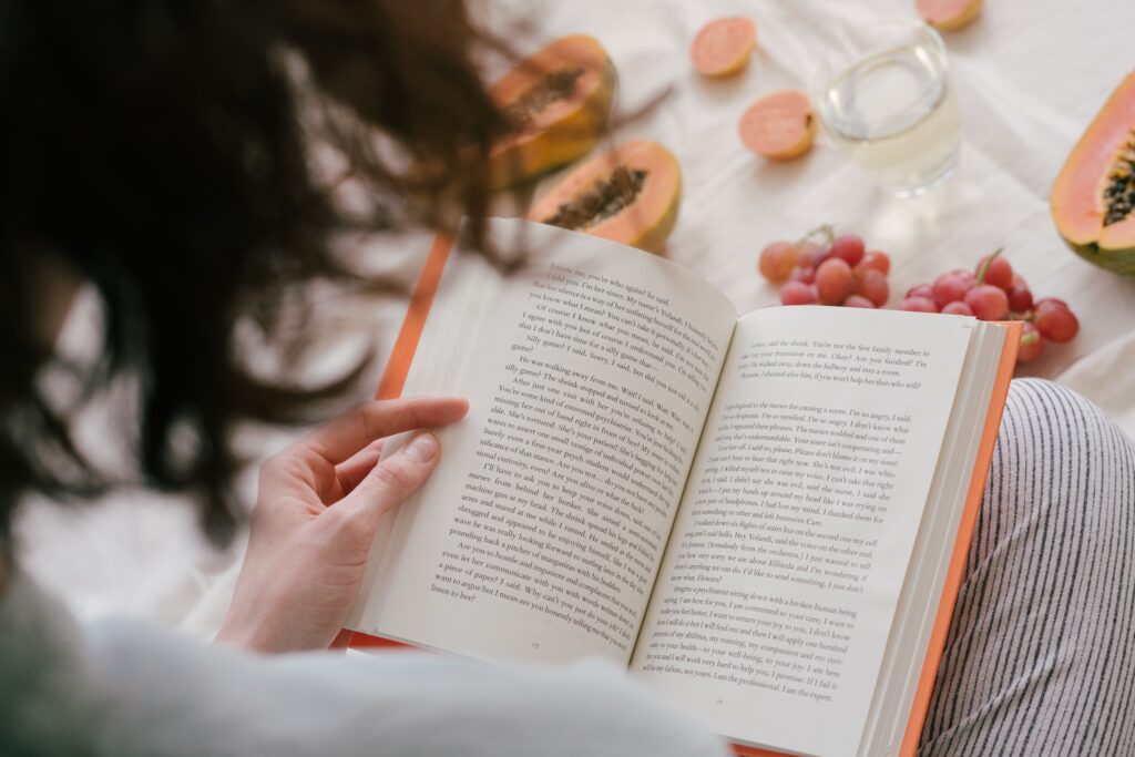 A person enjoys reading a book surrounded by fresh papaya, grapes, and a drink, creating a cozy indoor scene.